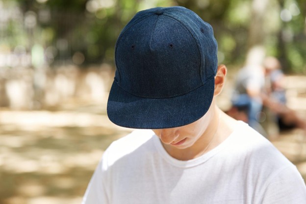 A close-up view of a schoolboy looking down, wearing a dark blue blank snapback.
