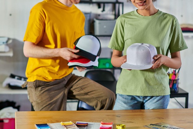 A cropped view of a smiling young African American crafts couple holding snapbacks they have made.