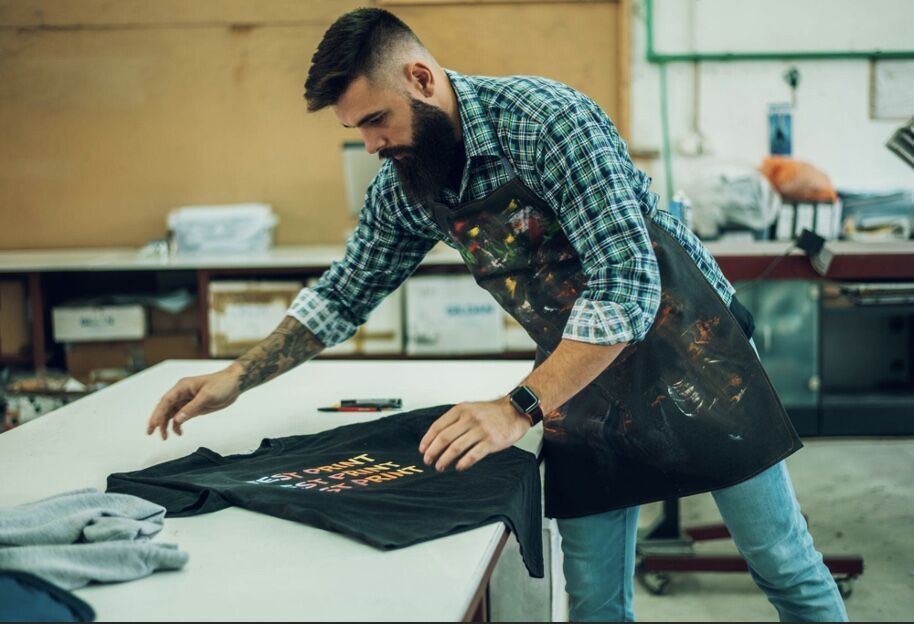 A male worker folds a freshly printed custom shirt in a printing workshop.