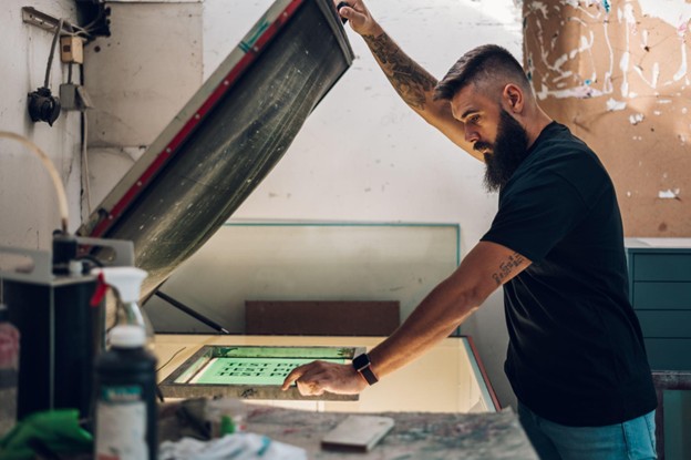 A male screen printing worker prepares stencils for precise, high-quality prints on a screen exposure unit.