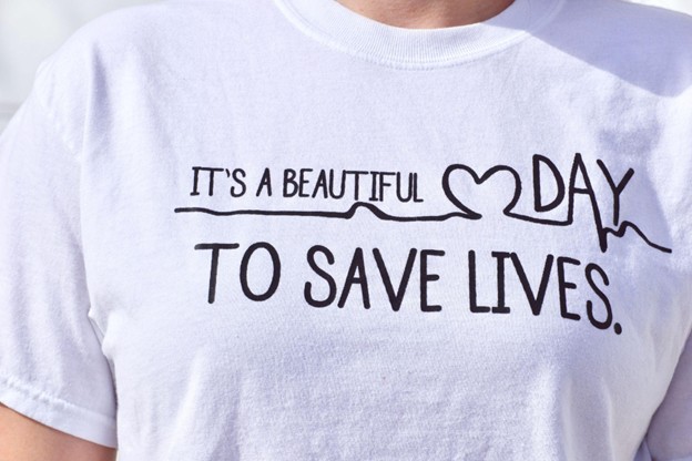 A close-up of a custom-designed shirt featuring the phrase "It's a beautiful day to save lives" along a heart rate monitor line on a white T-shirt.
