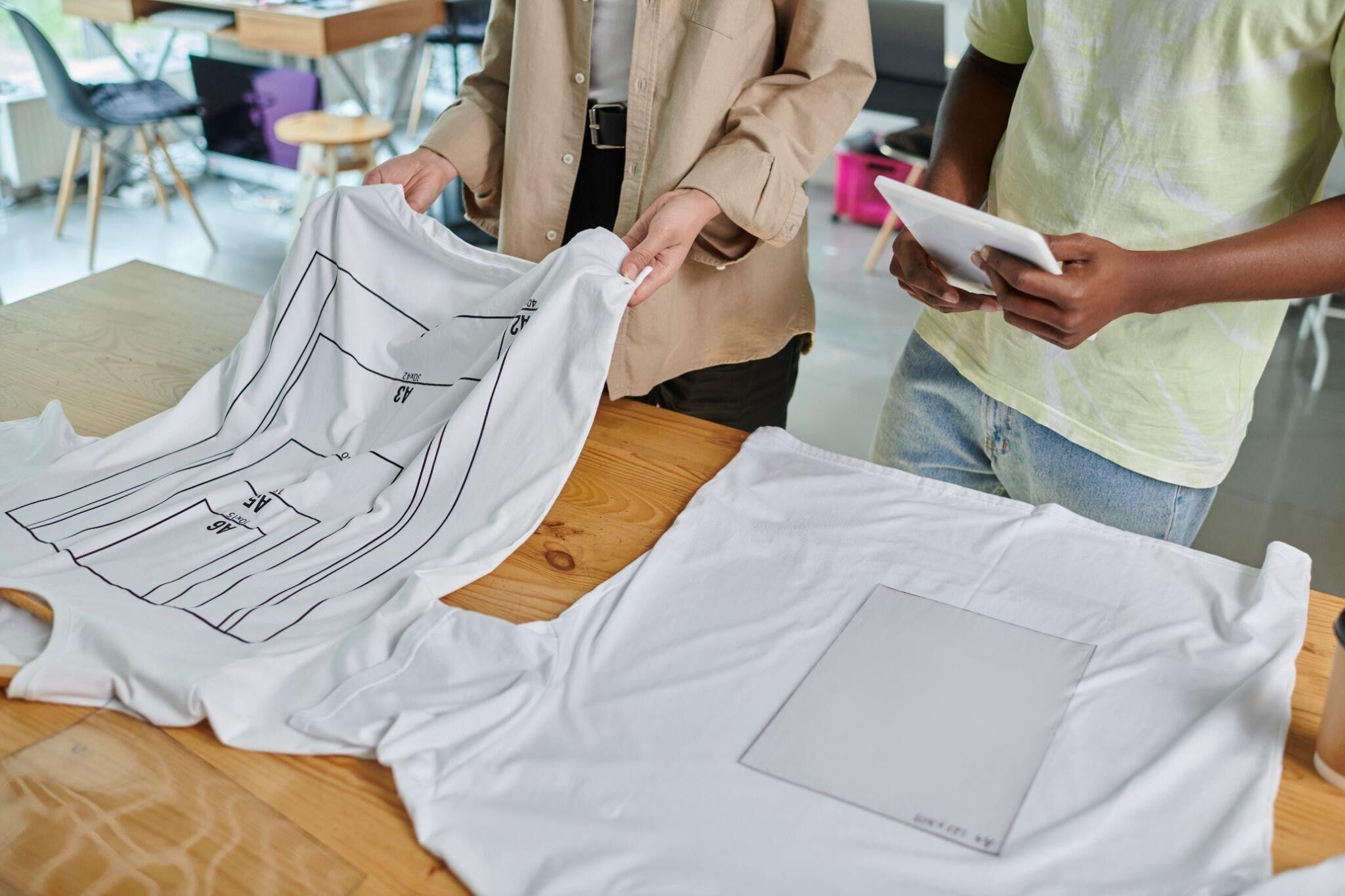A cropped view of a female designer showing the sizes of T-shirts to her male colleague. 
