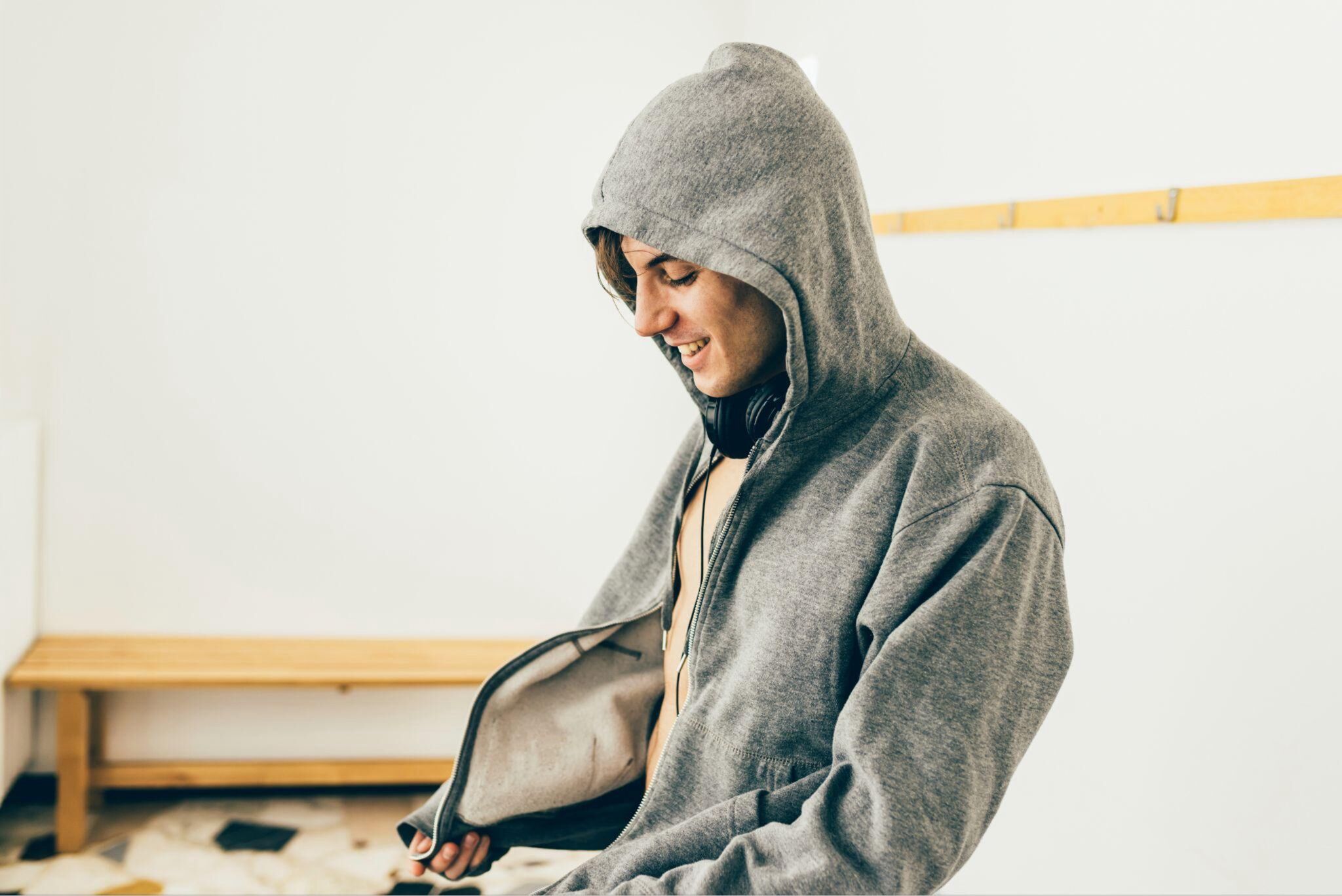 A man happily zips up his gray hoodie.